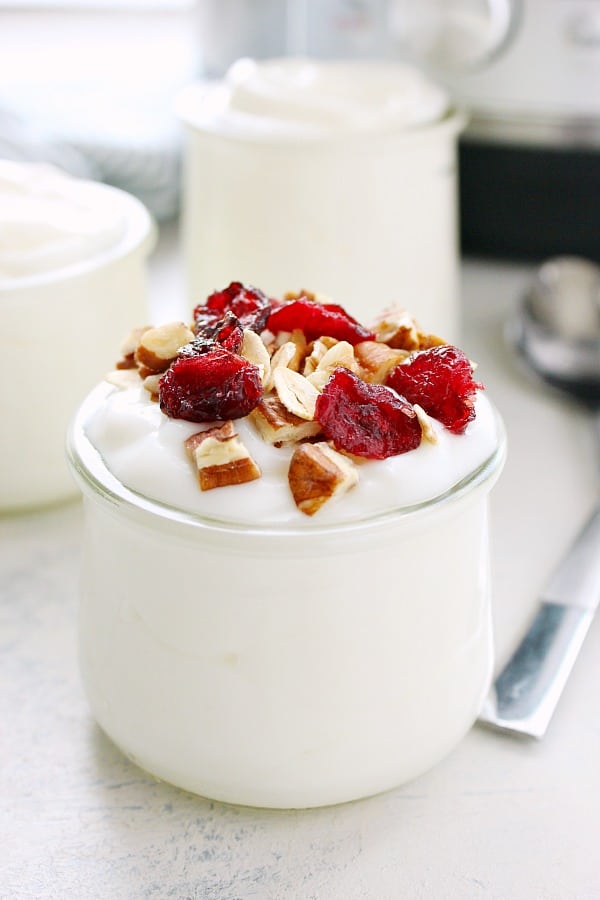 Yogurt in a small glass jar, with toppings, set on a gray board.