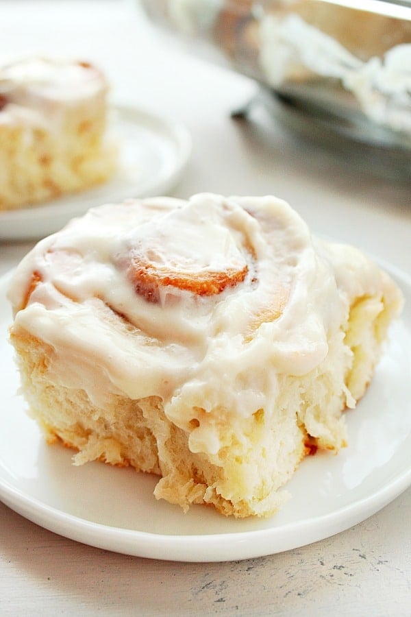 Cinnamon roll with cream cheese frosting on a white plate.