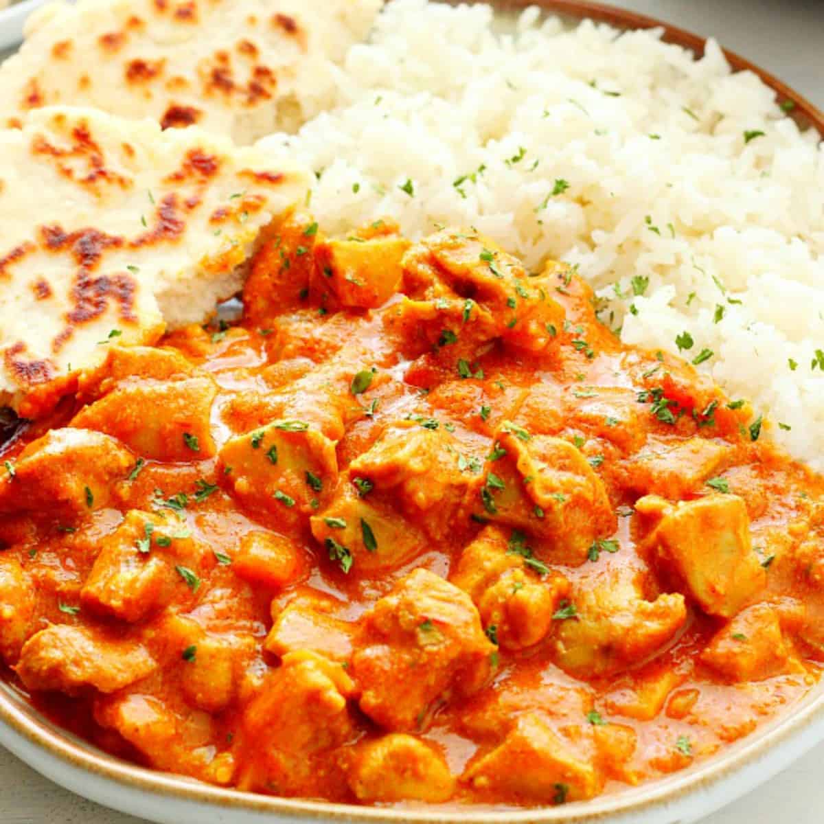 Butter chicken with rice and flatbread on plate.