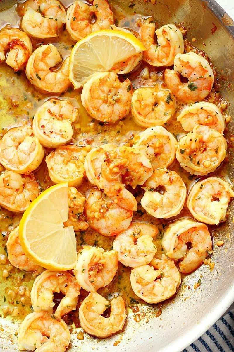 Cooked shrimp in garlic butter sauce with lemon in a skillet.