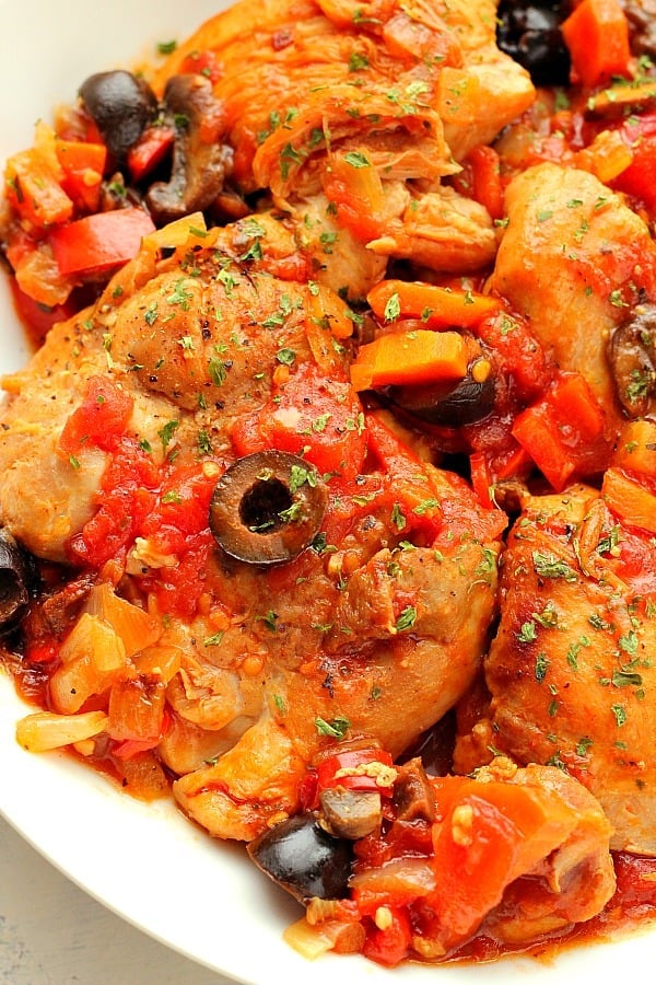 Chicken with tomato sauce, veggies on a white plate.