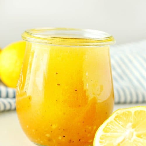 Salad dressing in a jar next to lemons.