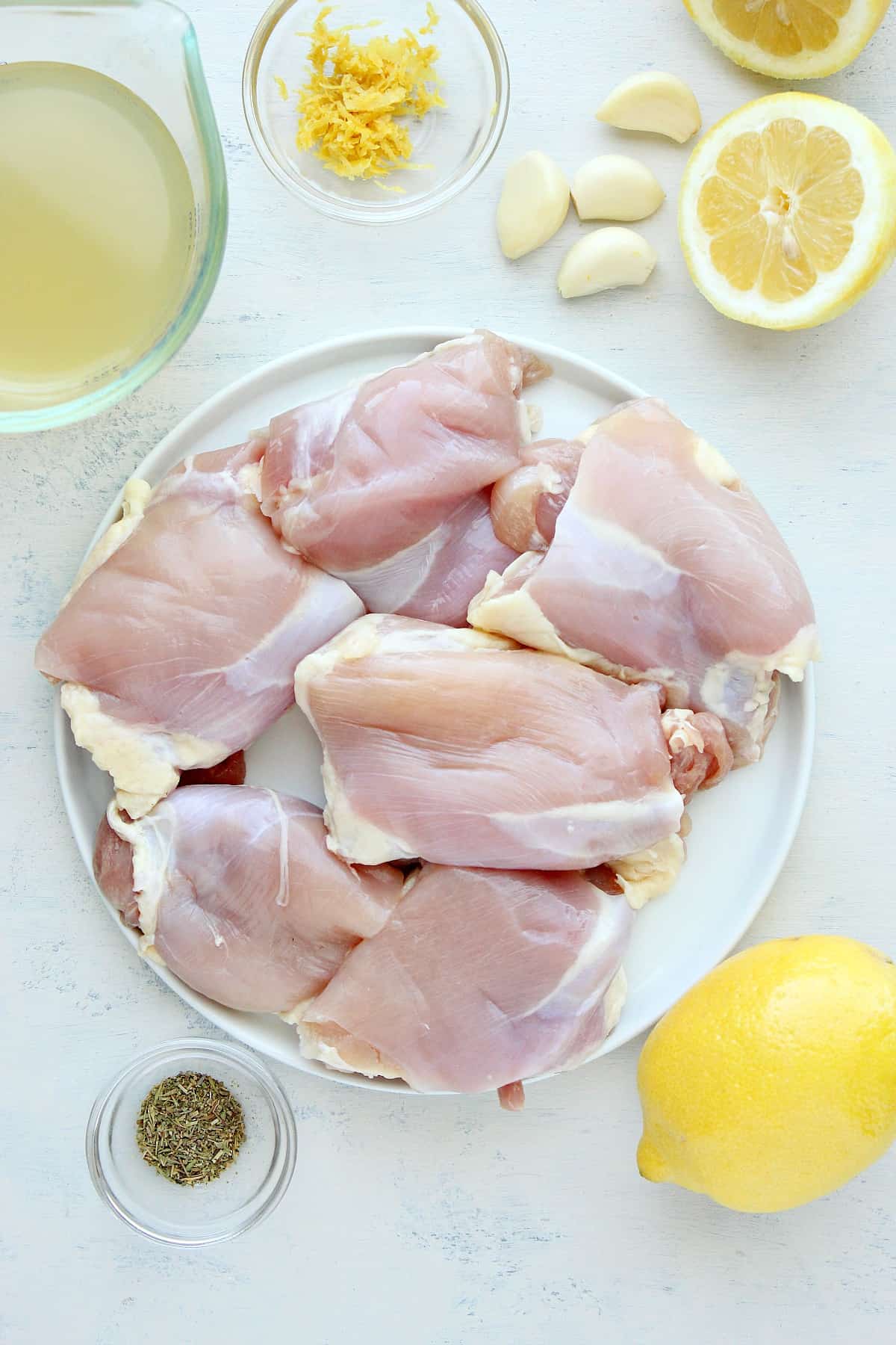 Chicken, seasoning and lemons on a white board.