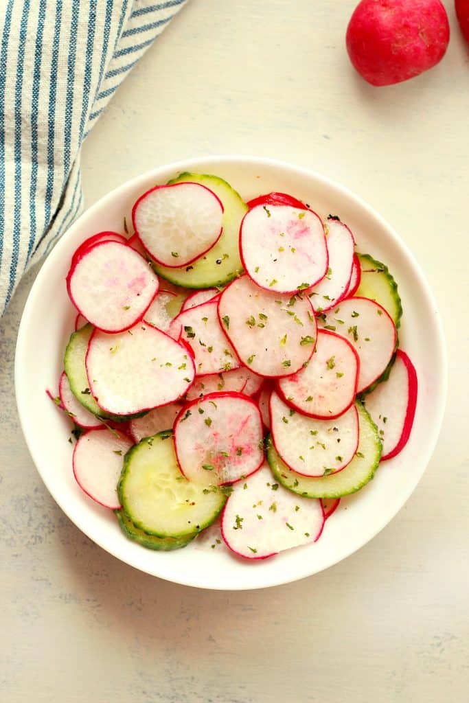 Salad with radishes, cucumber and onion in a white bowl.