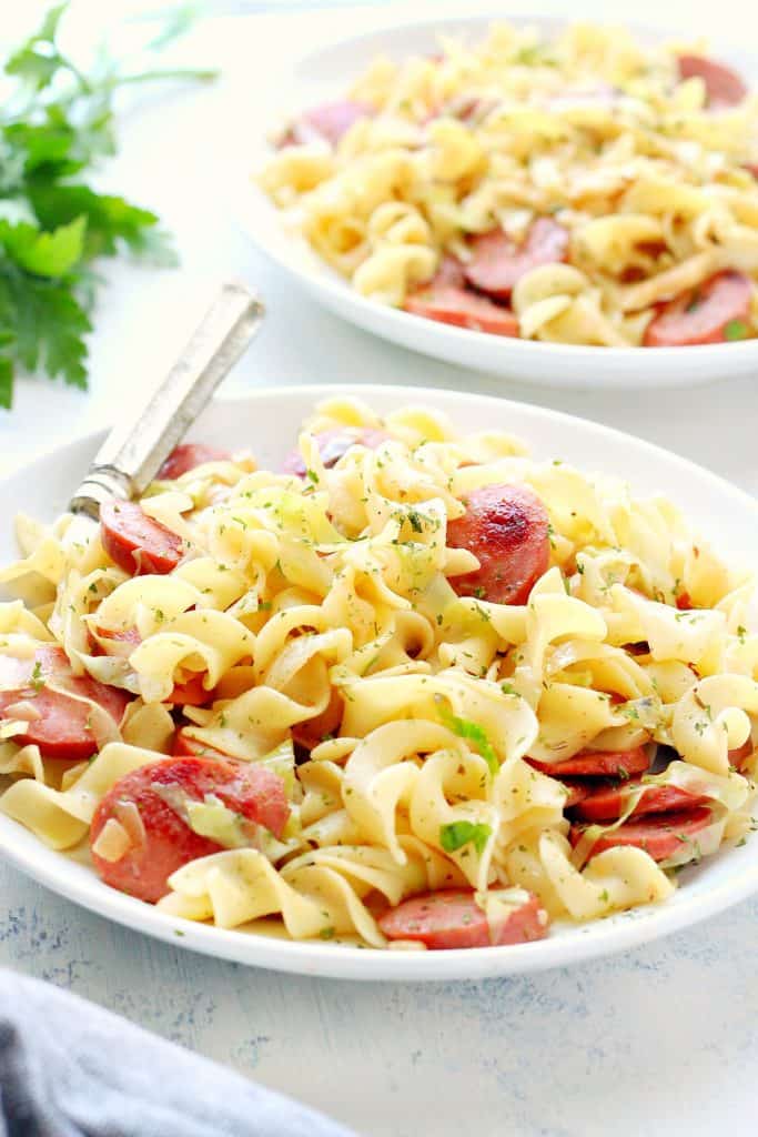 Cabbage and noodles with sausage on a white plate.