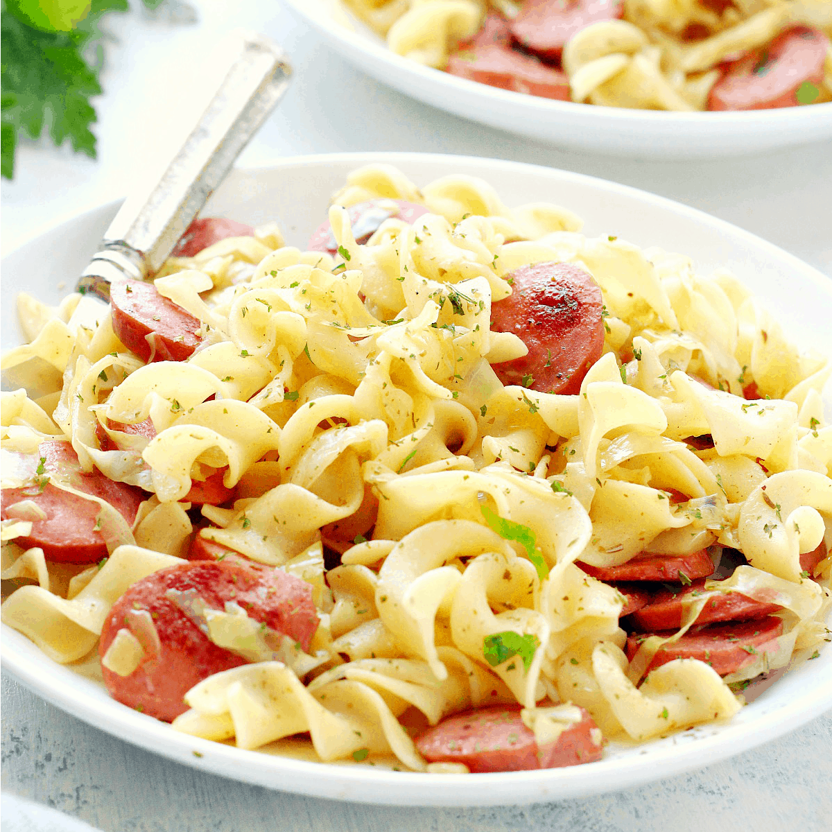 Wide noodles with cabbage and sausage on a plate.