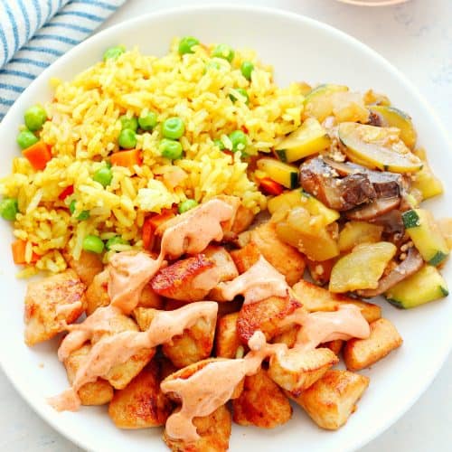 Chicken, fried rice and sauteed veggies on a plate.
