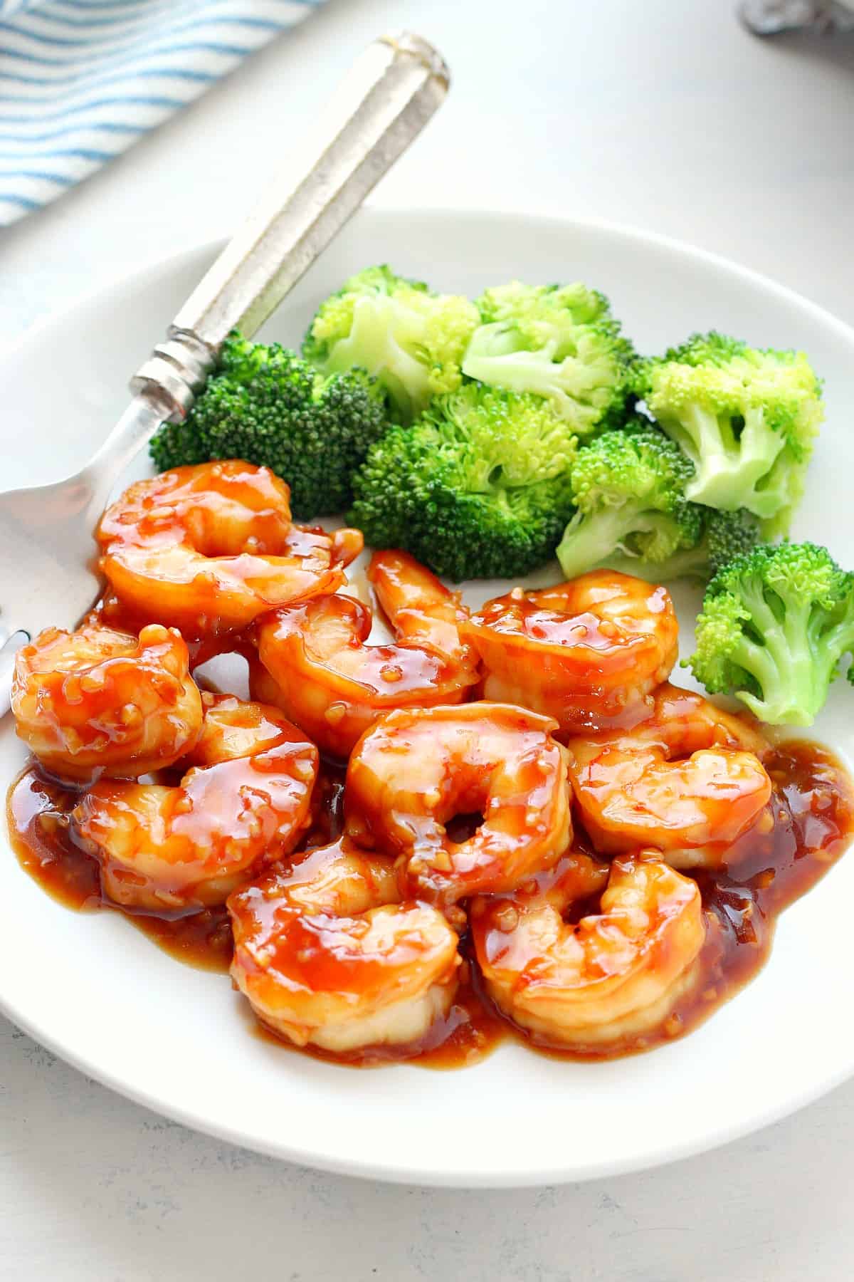 Shrimp with sauce and broccoli on a white plate.