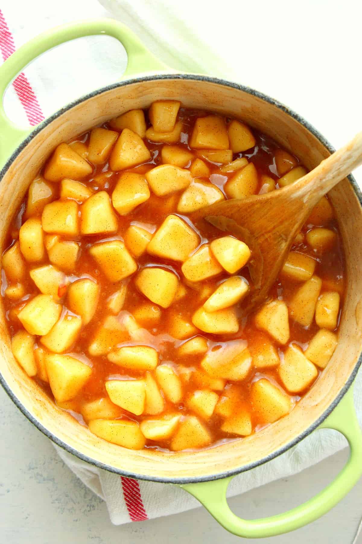 Apple pie filling in a Dutch oven with wooden spoon.