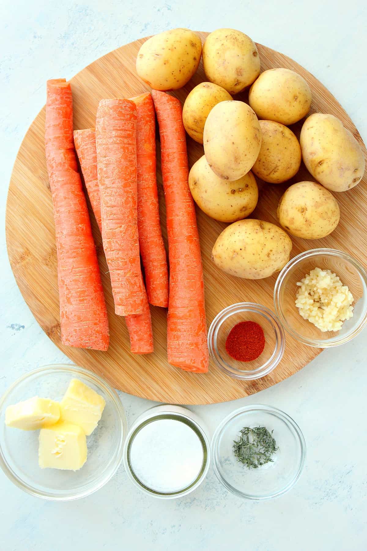 Baby potatoes and carrots on a round cutting board.
