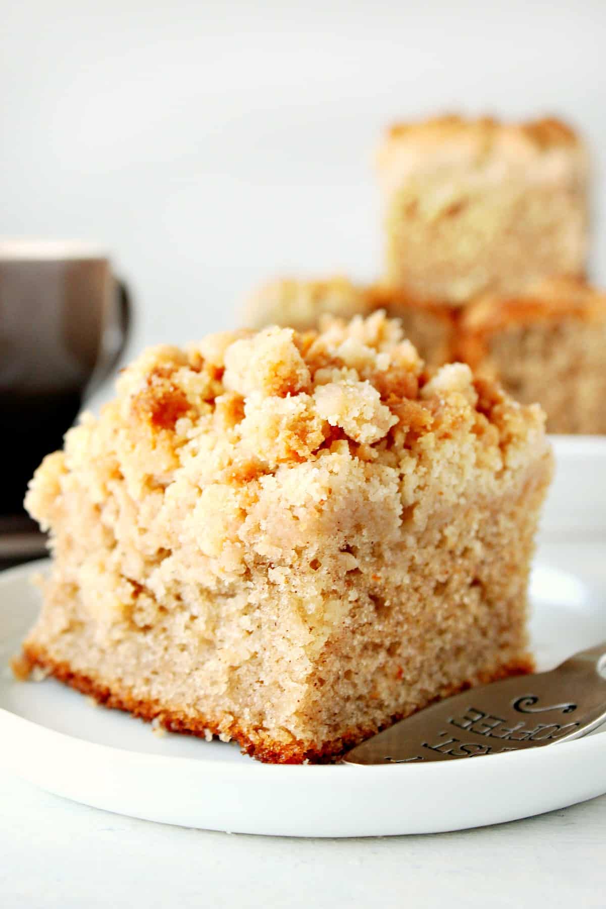 Crumb cake on a white dessert plate with a spoon.