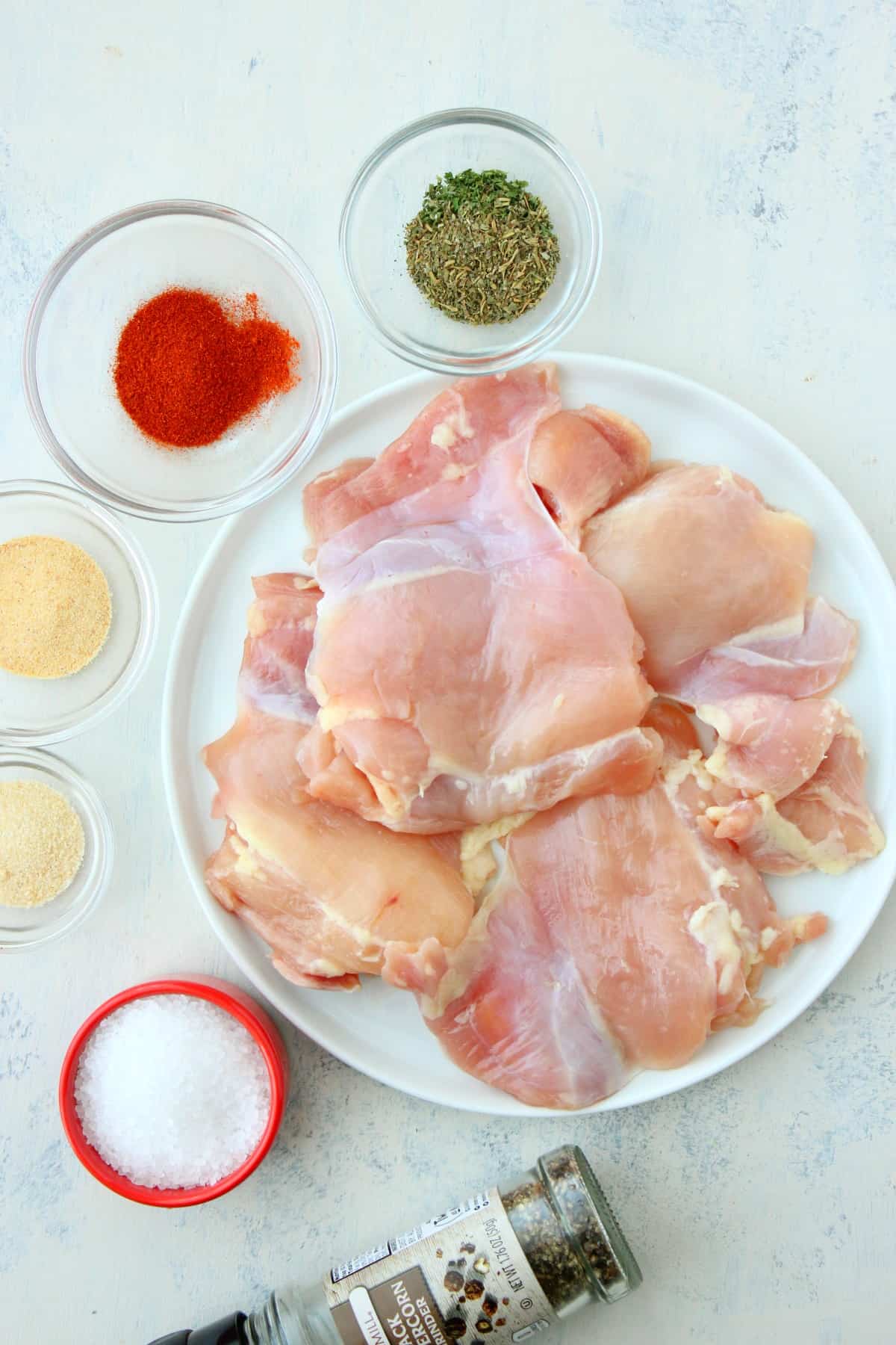 Chicken thighs and spices on a white board.