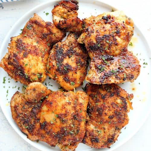 Cooked chicken thighs on a white plate.