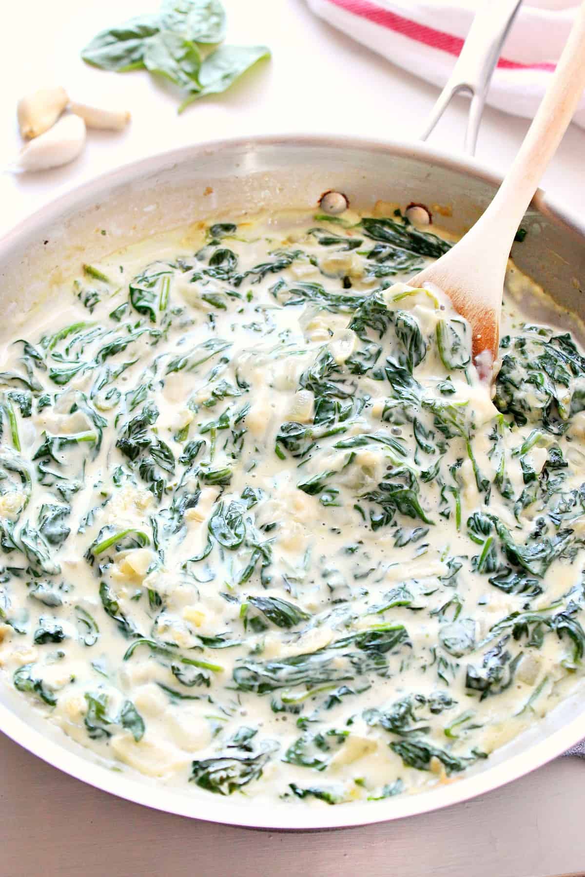 Creamy spinach in a skillet with wooden spoon.