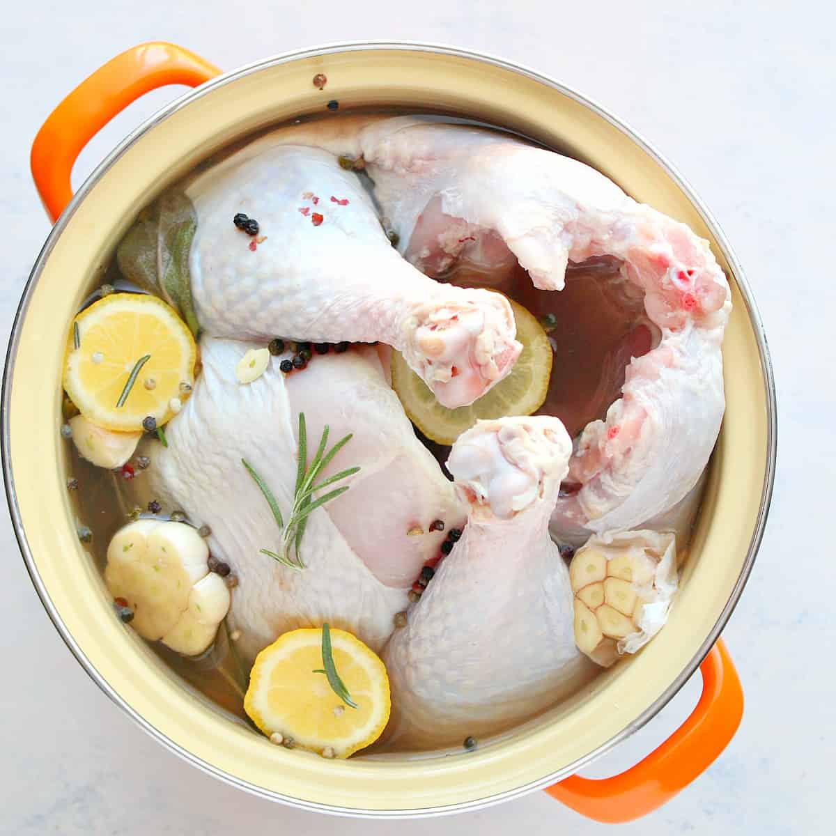 Turkey submerged in a pot with brine, herbs and lemon slices.