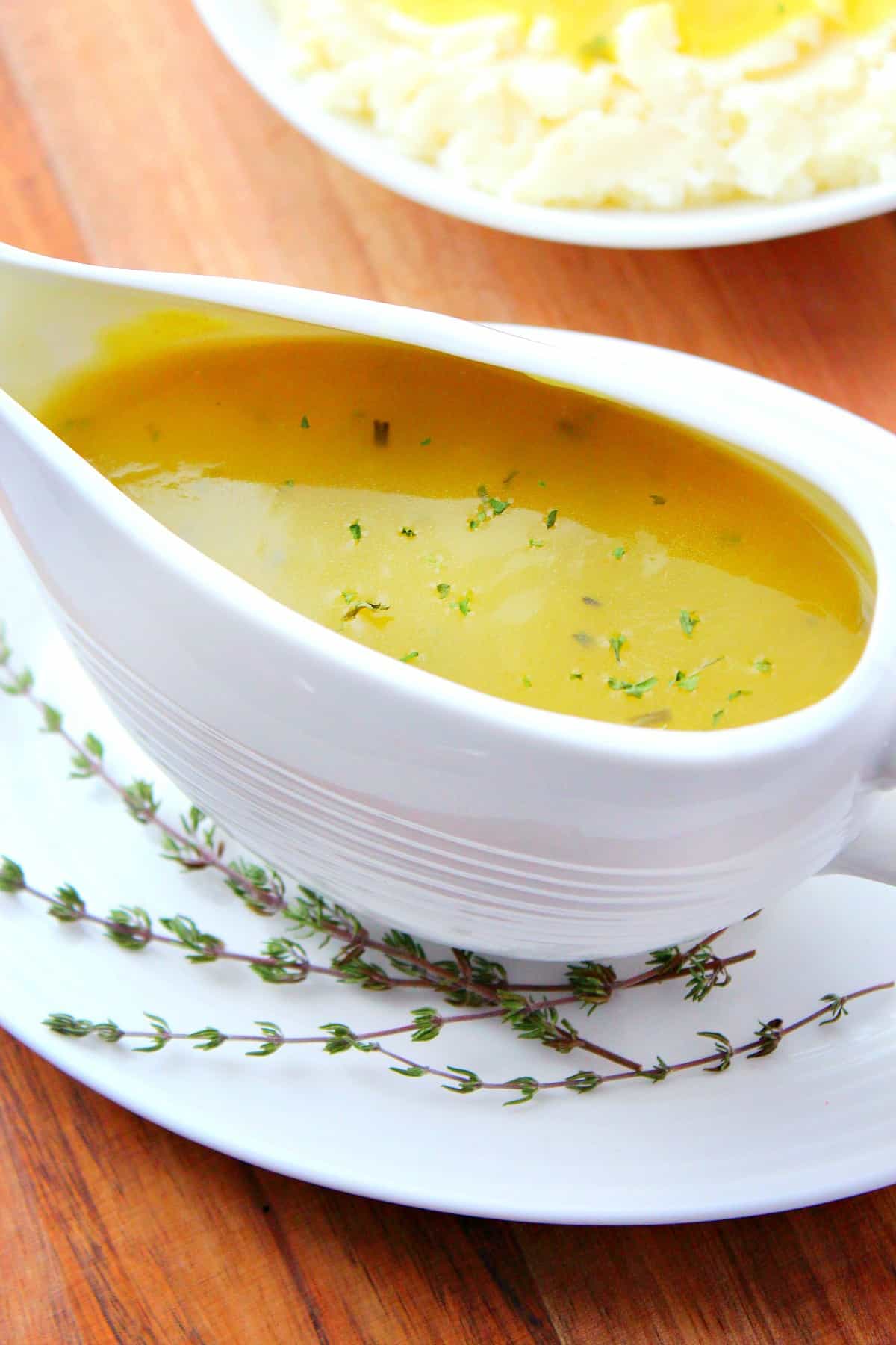 Easy Turkey Gravy recipe Gravy in a white gravy boat on a wooden cutting board.