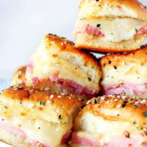 Sliders with ham and cheese stacked on a plate.