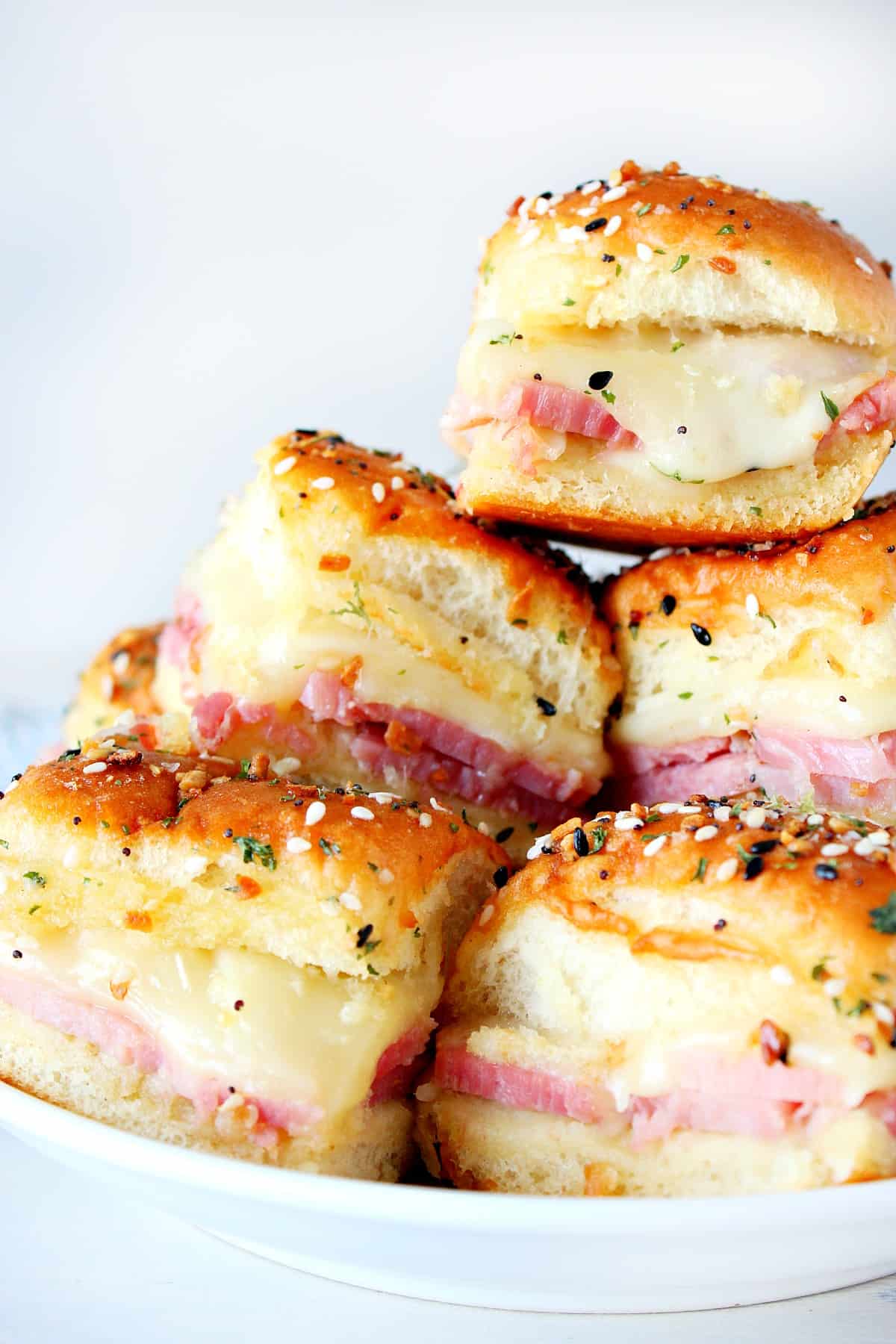 Sliders with ham and cheese stacked on a plate.