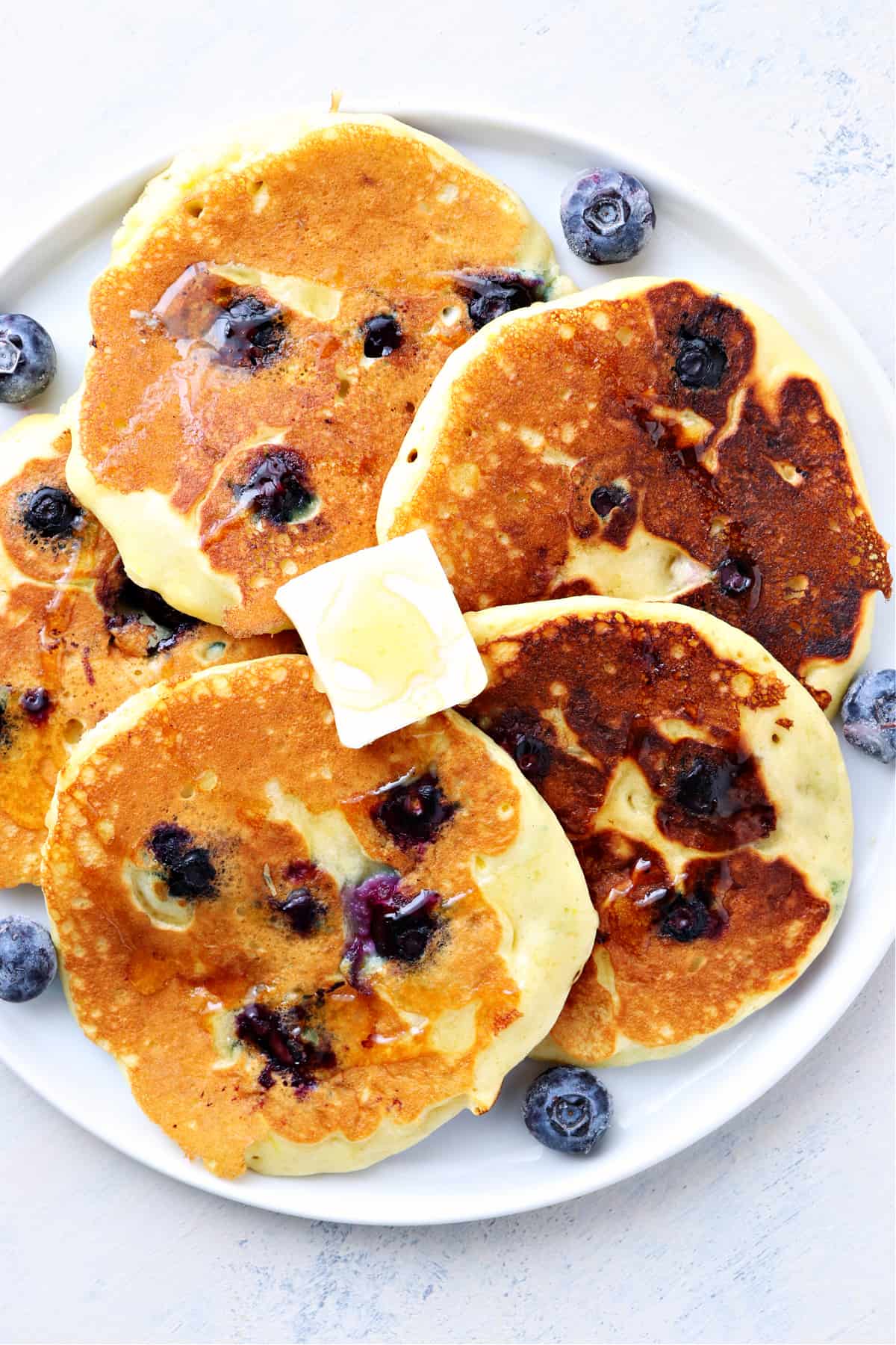 Five pancakes with honey and blueberries on a plate.