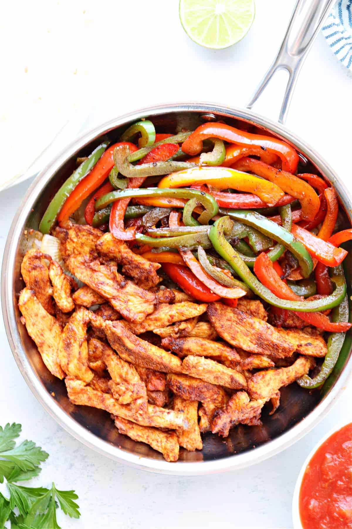 Skillet with cooked chicken and bell peppers, on a marble board.