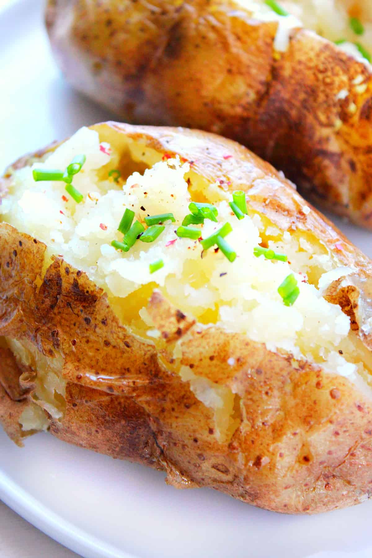 Baked potato with butter and chives on a plate.