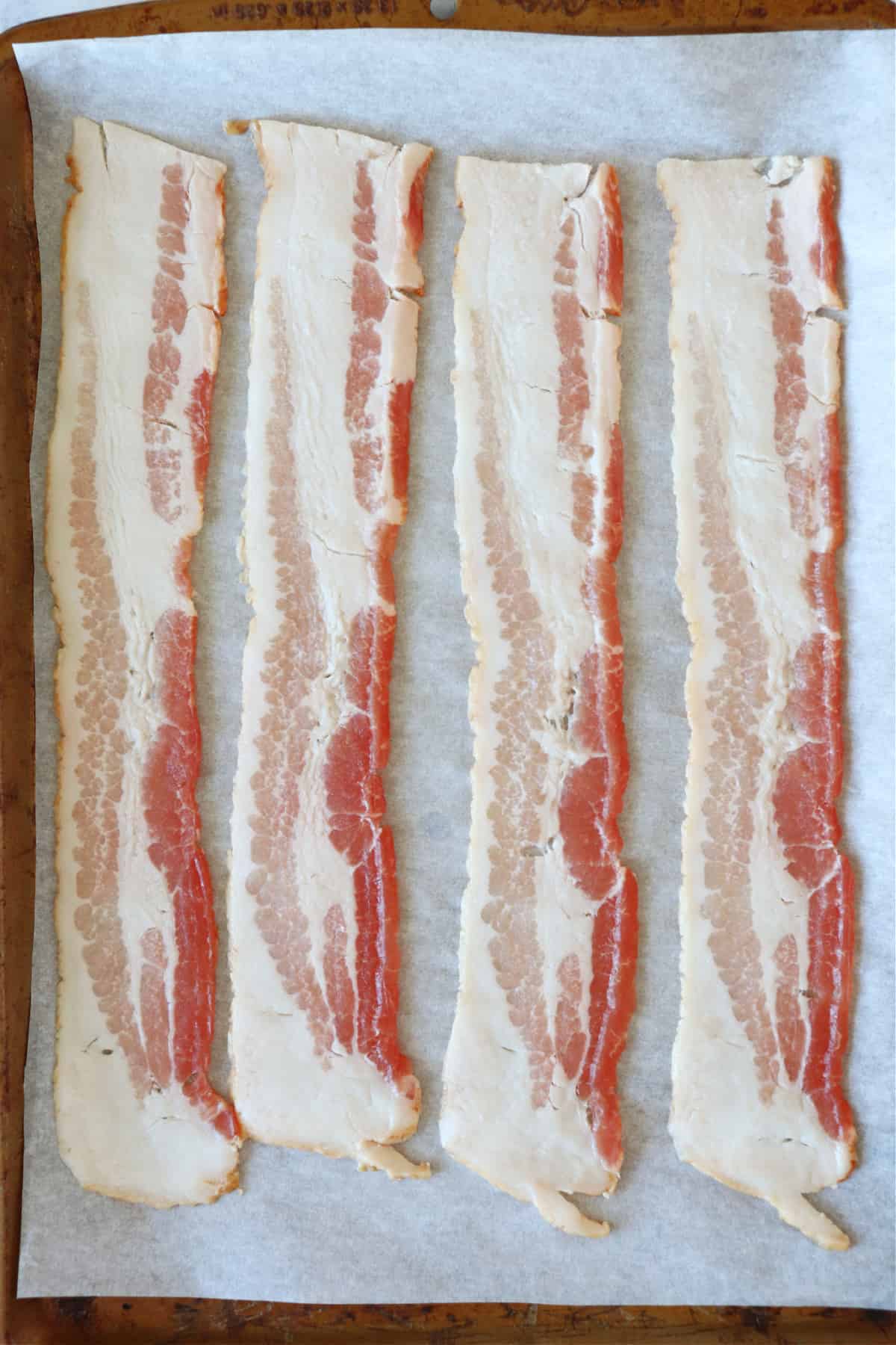 Raw bacon strips on a baking sheet.