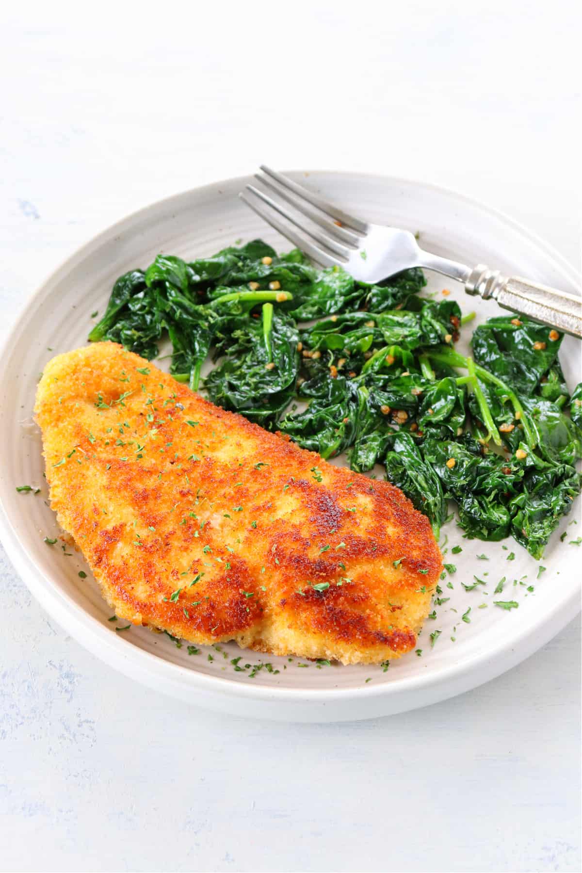 Breaded and fried chicken piece with sauteed spinach on a plate.