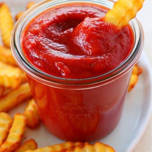 Ketchup in a jar with fries around.