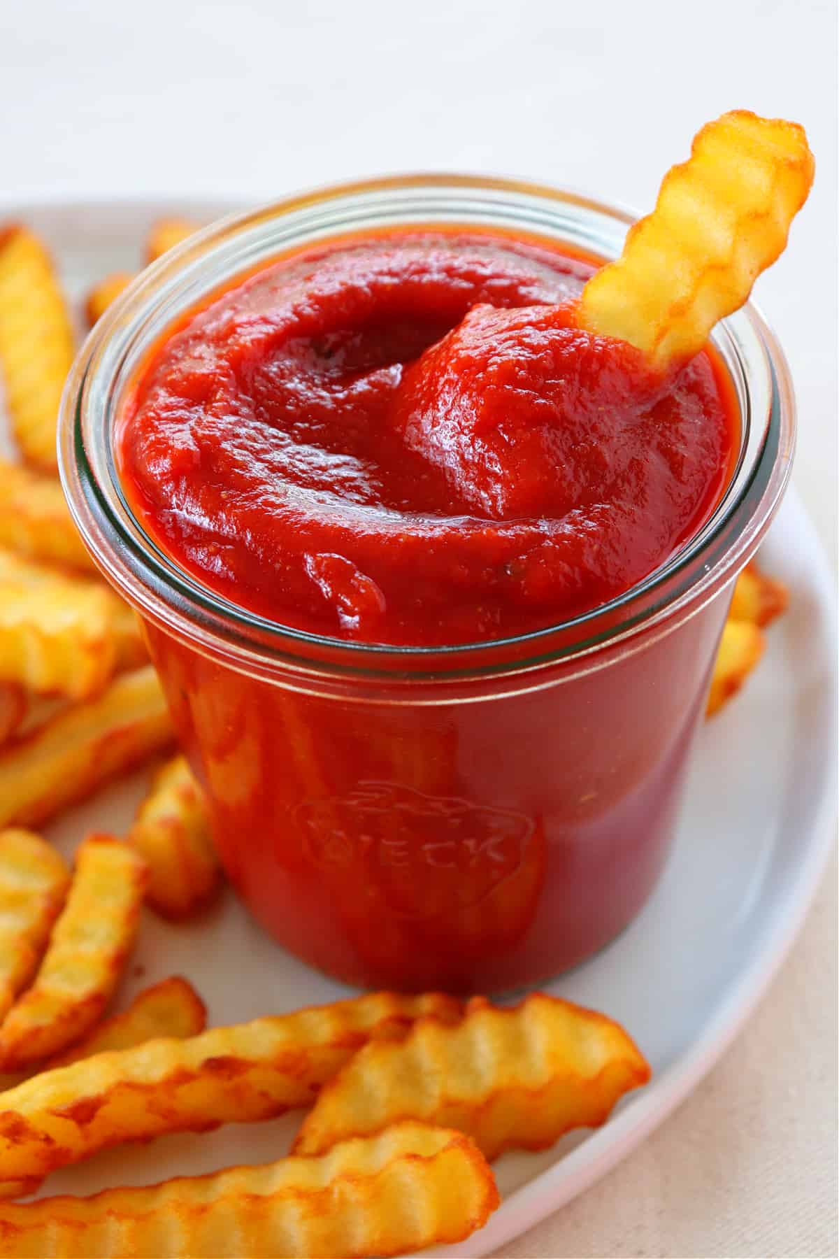 Ketchup in a jar with fries around.