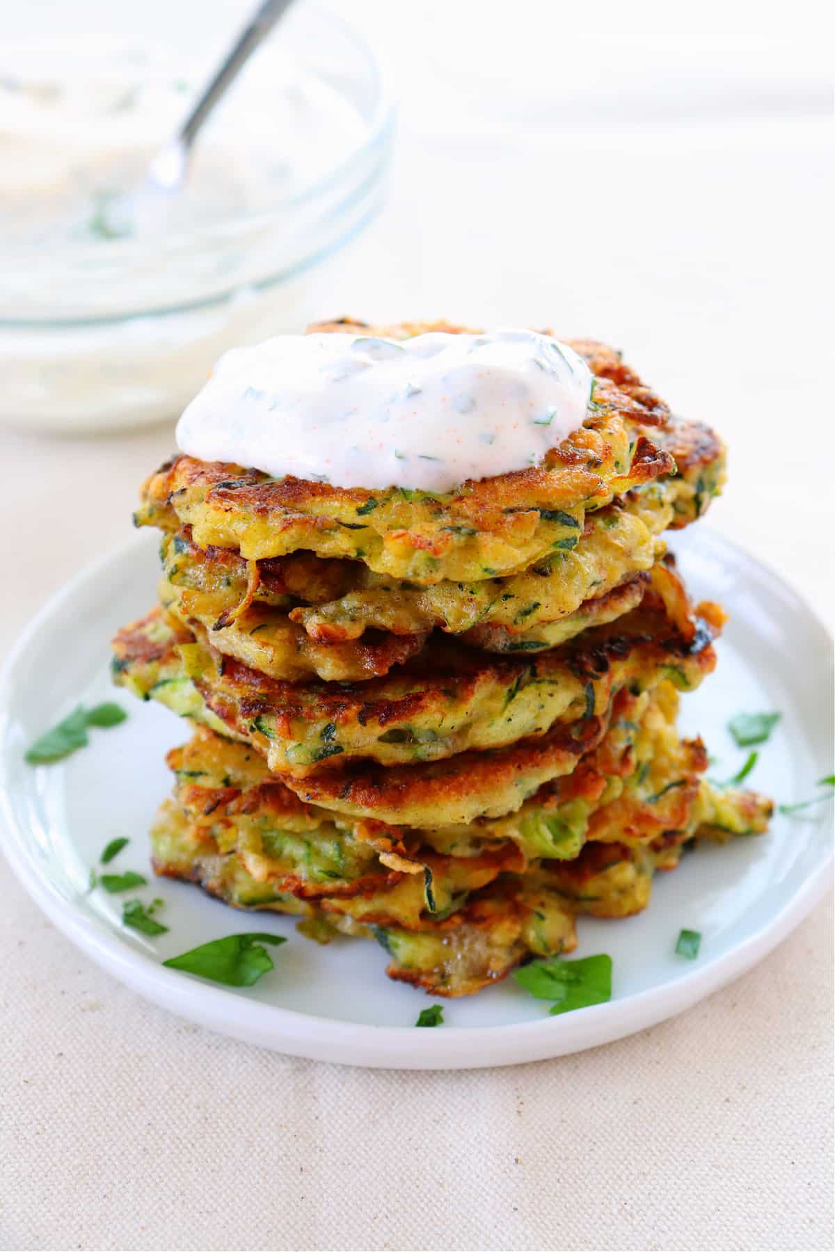 Stack of zucchini fritters with topping on a plate.