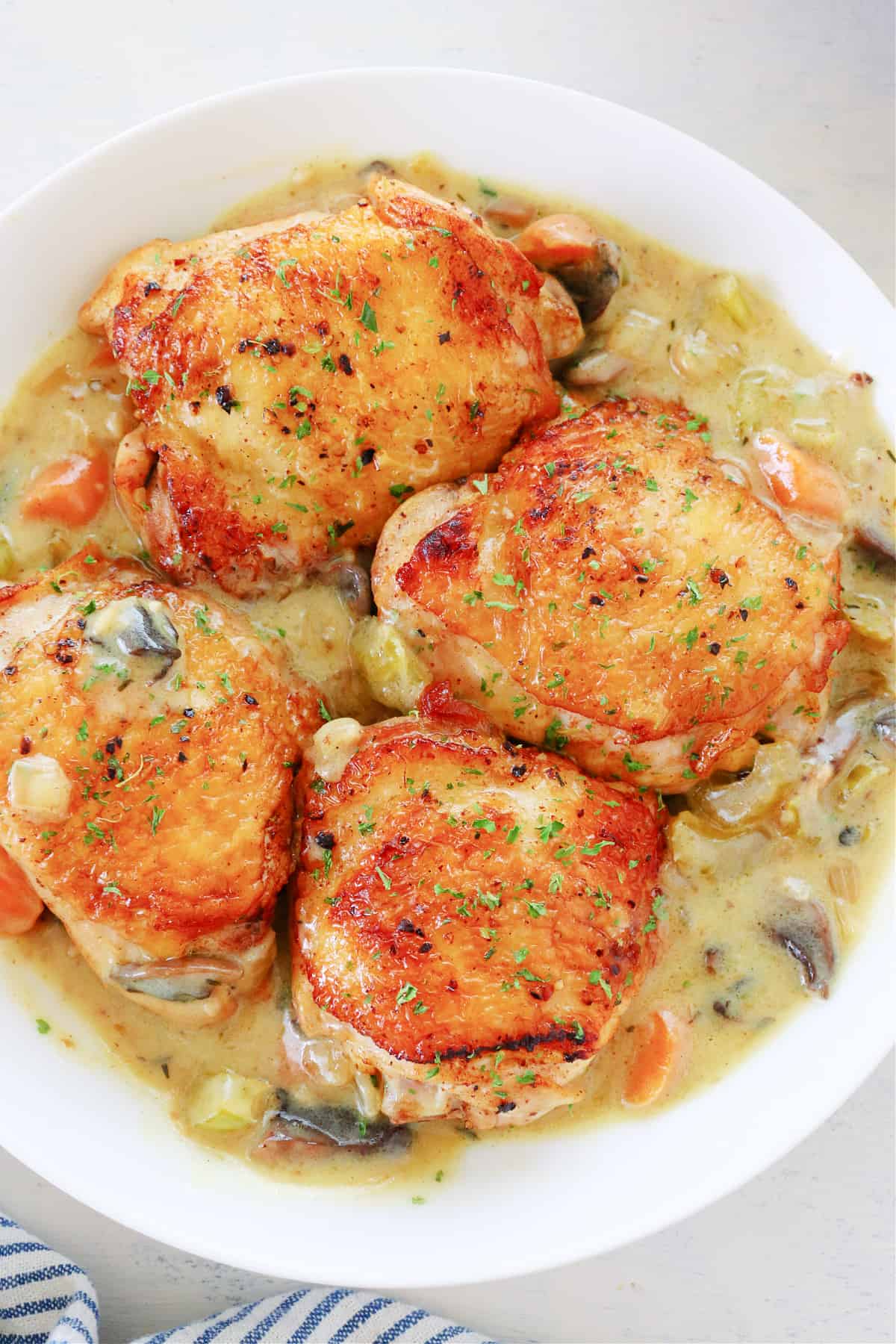 Chicken thighs with veggie sauce in serving dish.