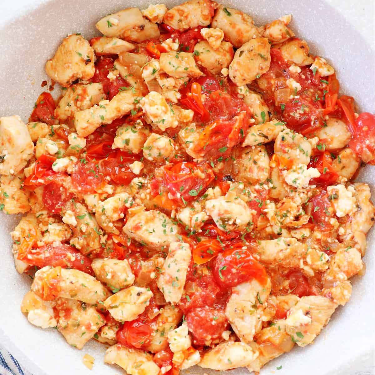 Chicken with tomatoes and feta in a skillet.