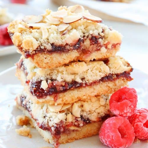 Stacked raspberry jam streusel bars on a plate.