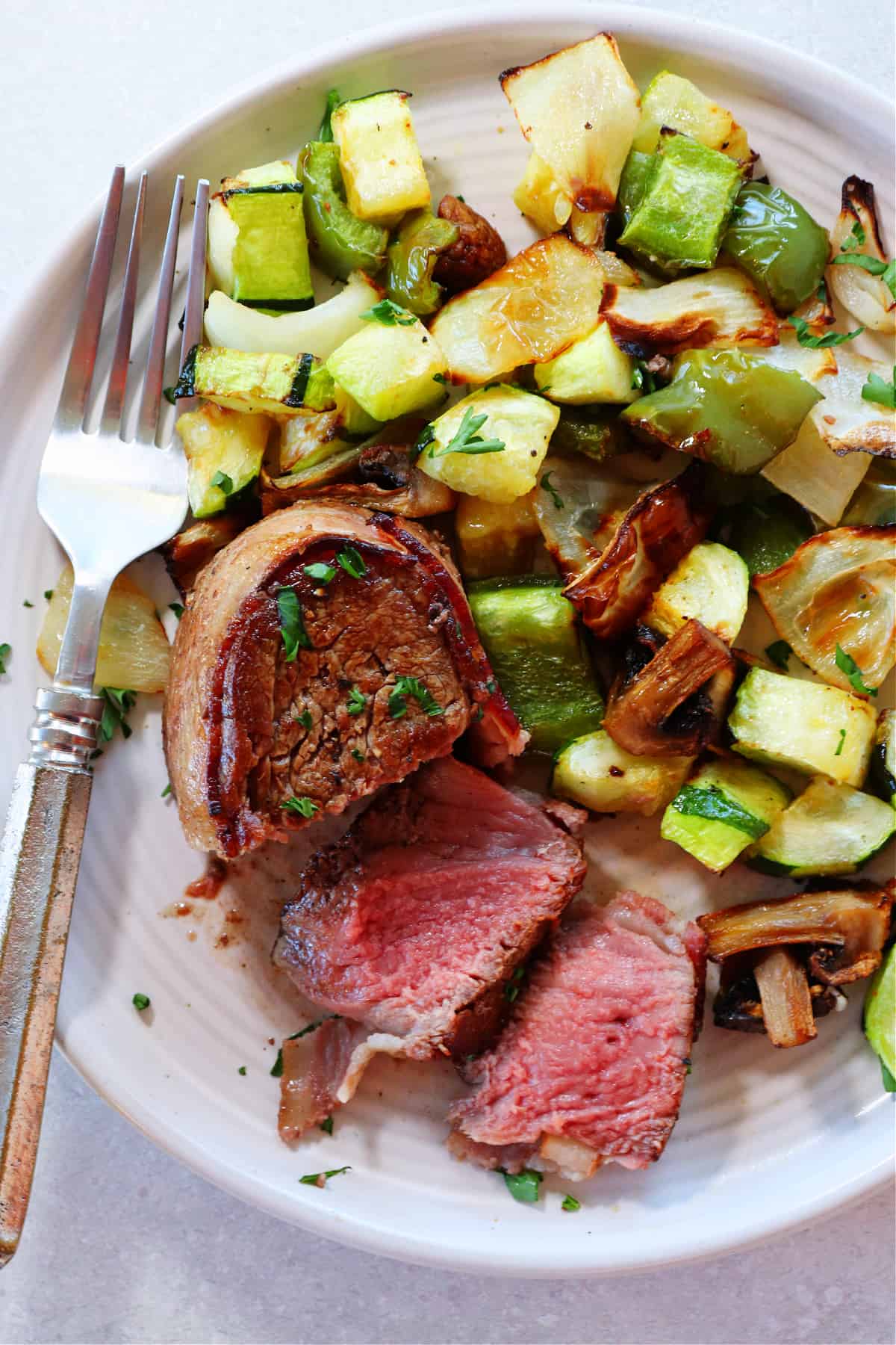 Sliced filet mignon with bacon and vegetables on a plate.