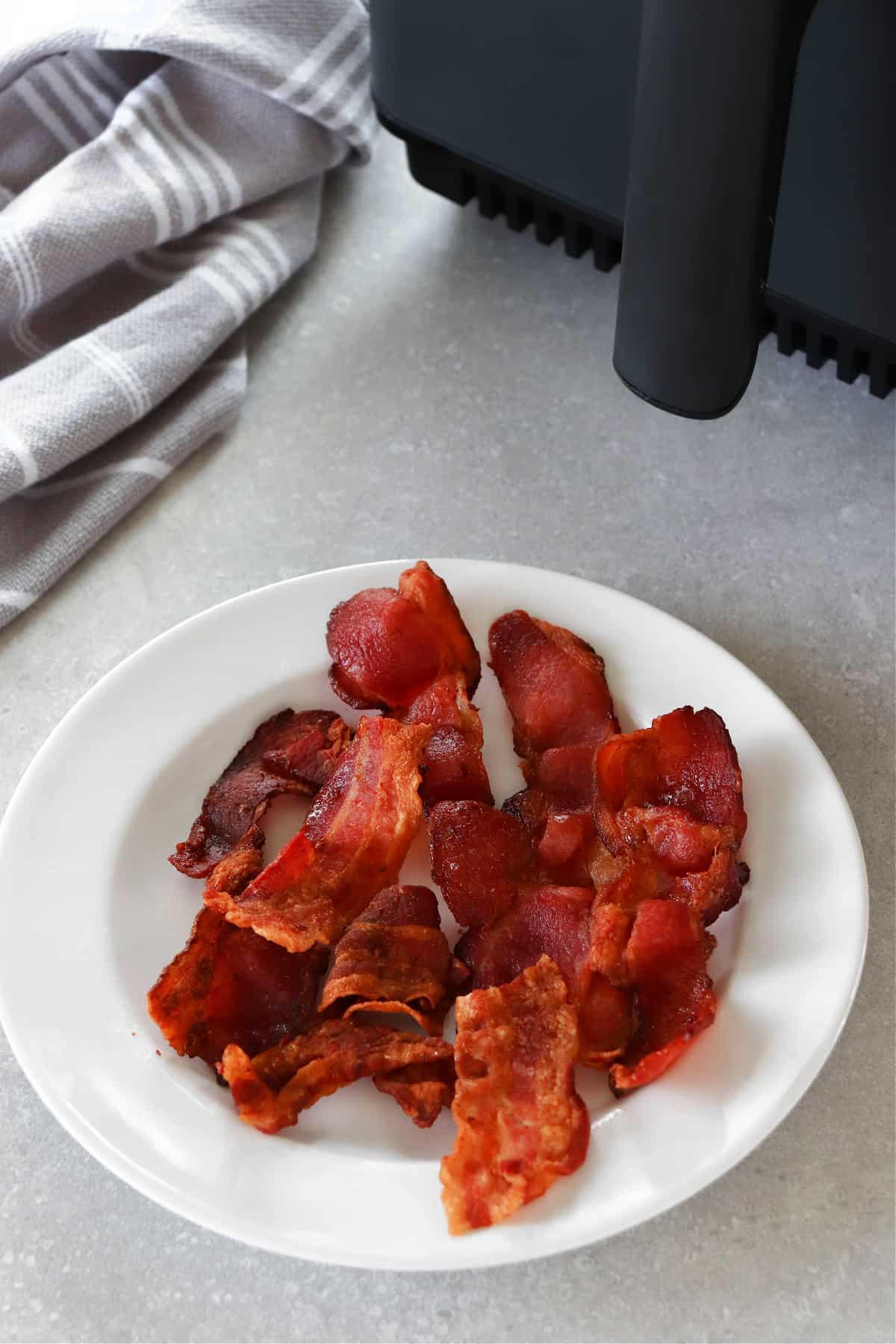 Air Fryer Bacon recipe Bacon on a plate next to the air fryer.