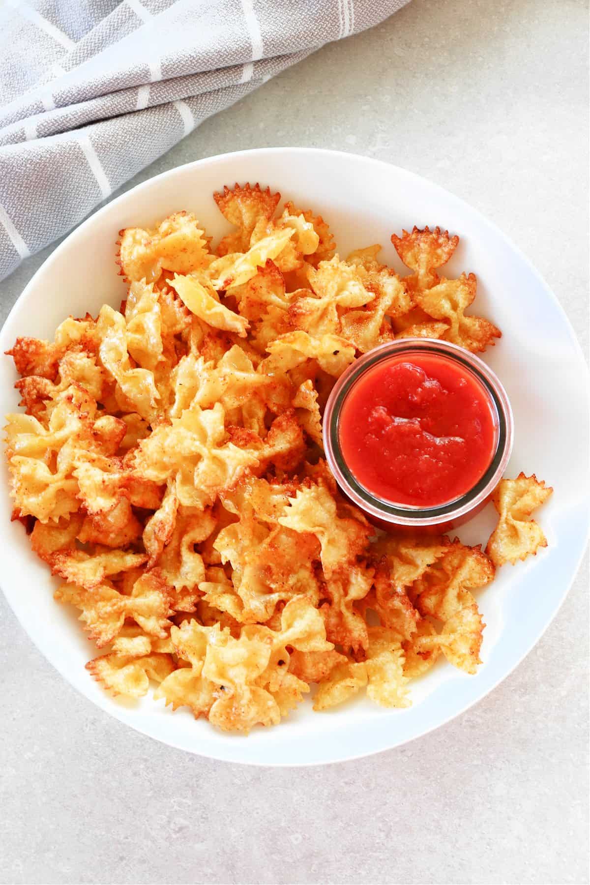 Pasta chips in a white bowl with marinara sauce in a cup.