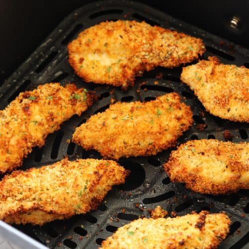 Chicken tenders in an air fryer basket.