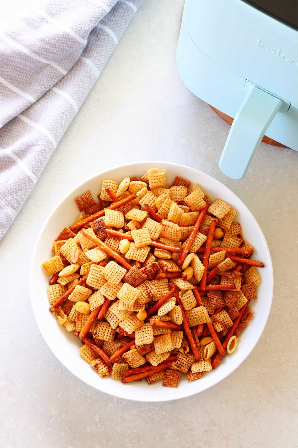 Air Fryer Party Mix recipe Party mix in white bowl next to air fryer.