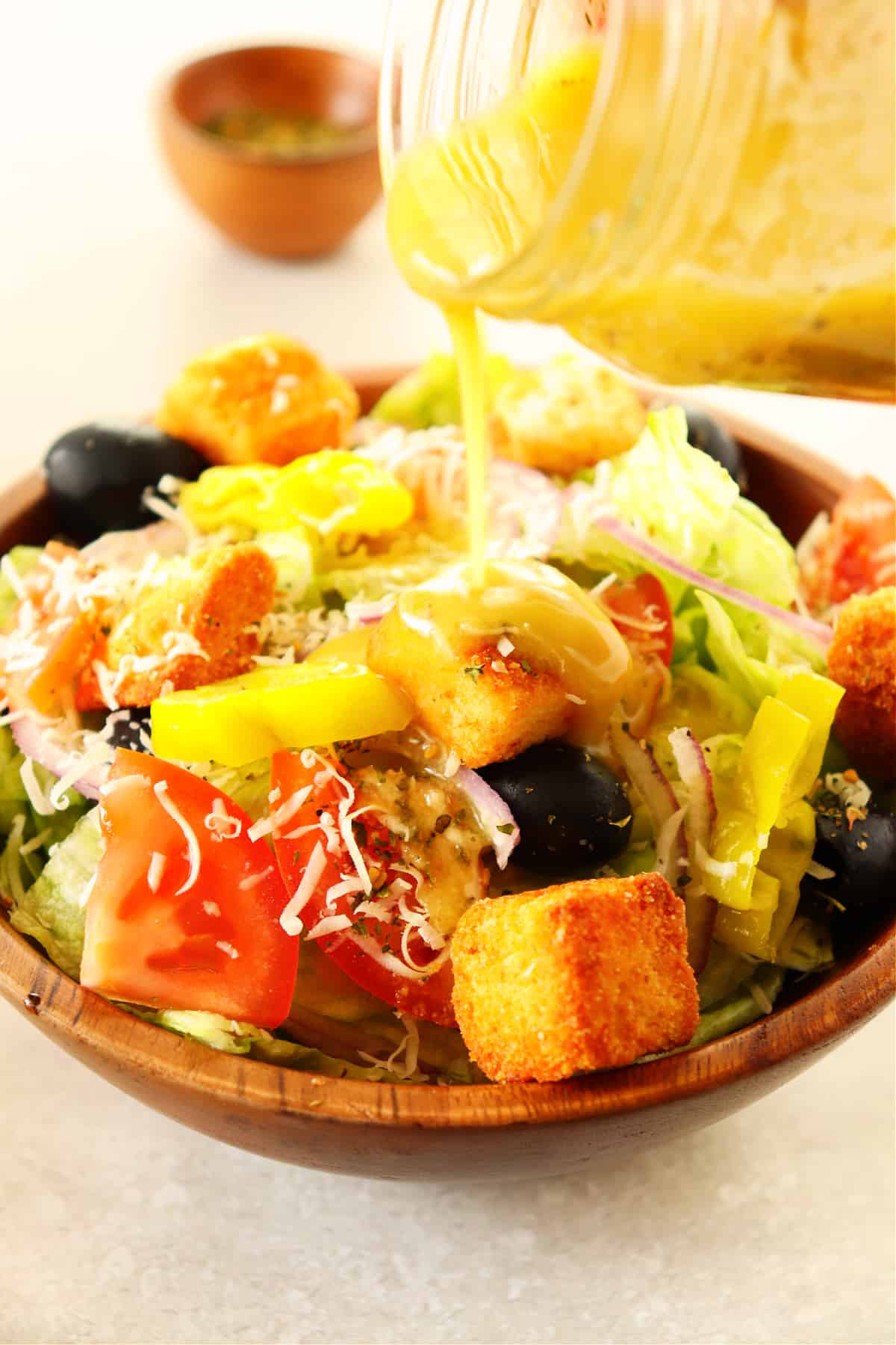 Salad in a wooden bowl with dressing poured from a jar.