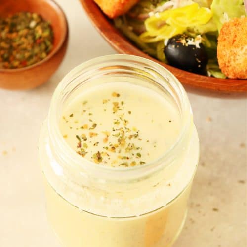 Creamy dressing in a glass jar next to a bowl with salad.