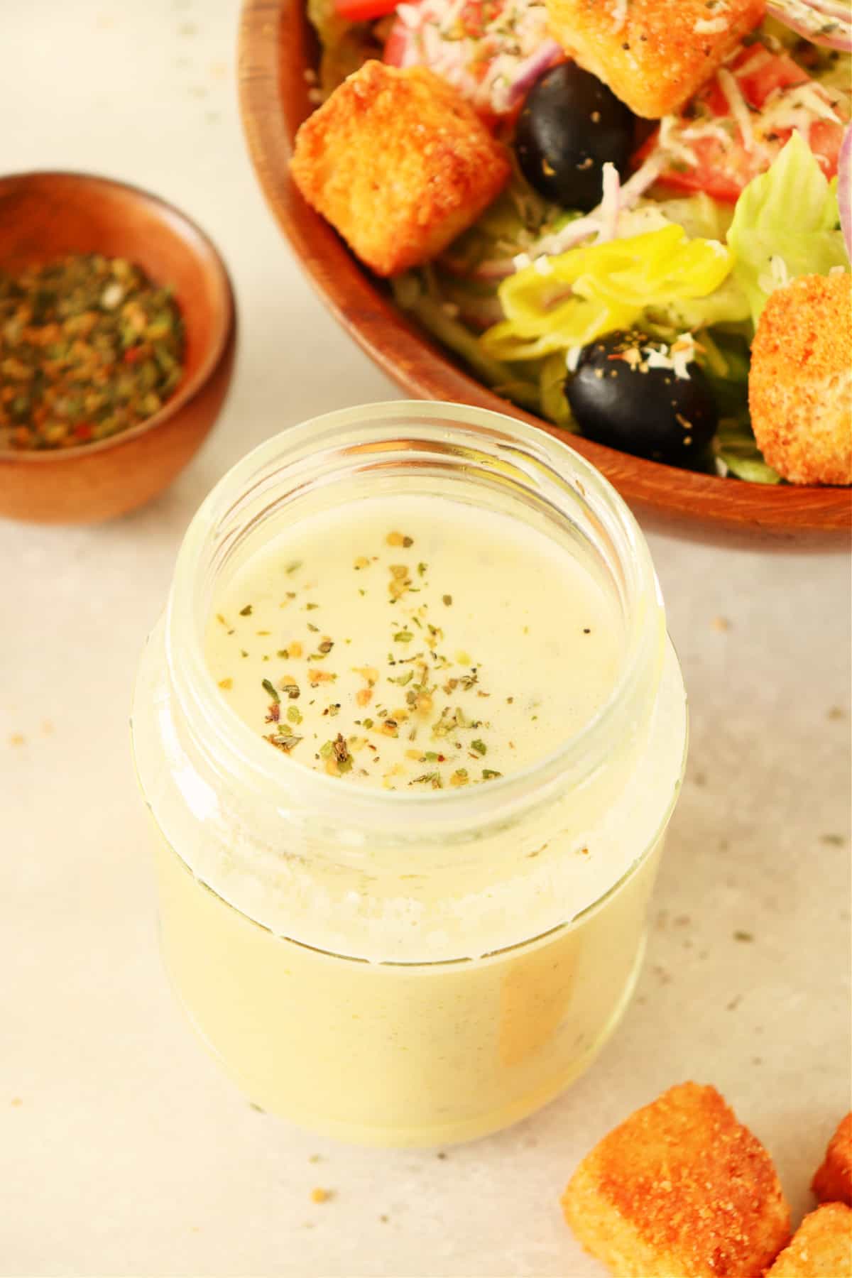 Creamy dressing in a glass jar next to a bowl with salad.