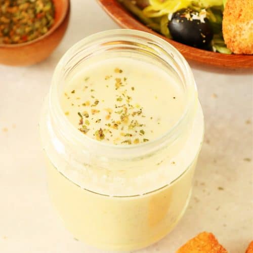 Creamy dressing in a small jar, next to a salad.