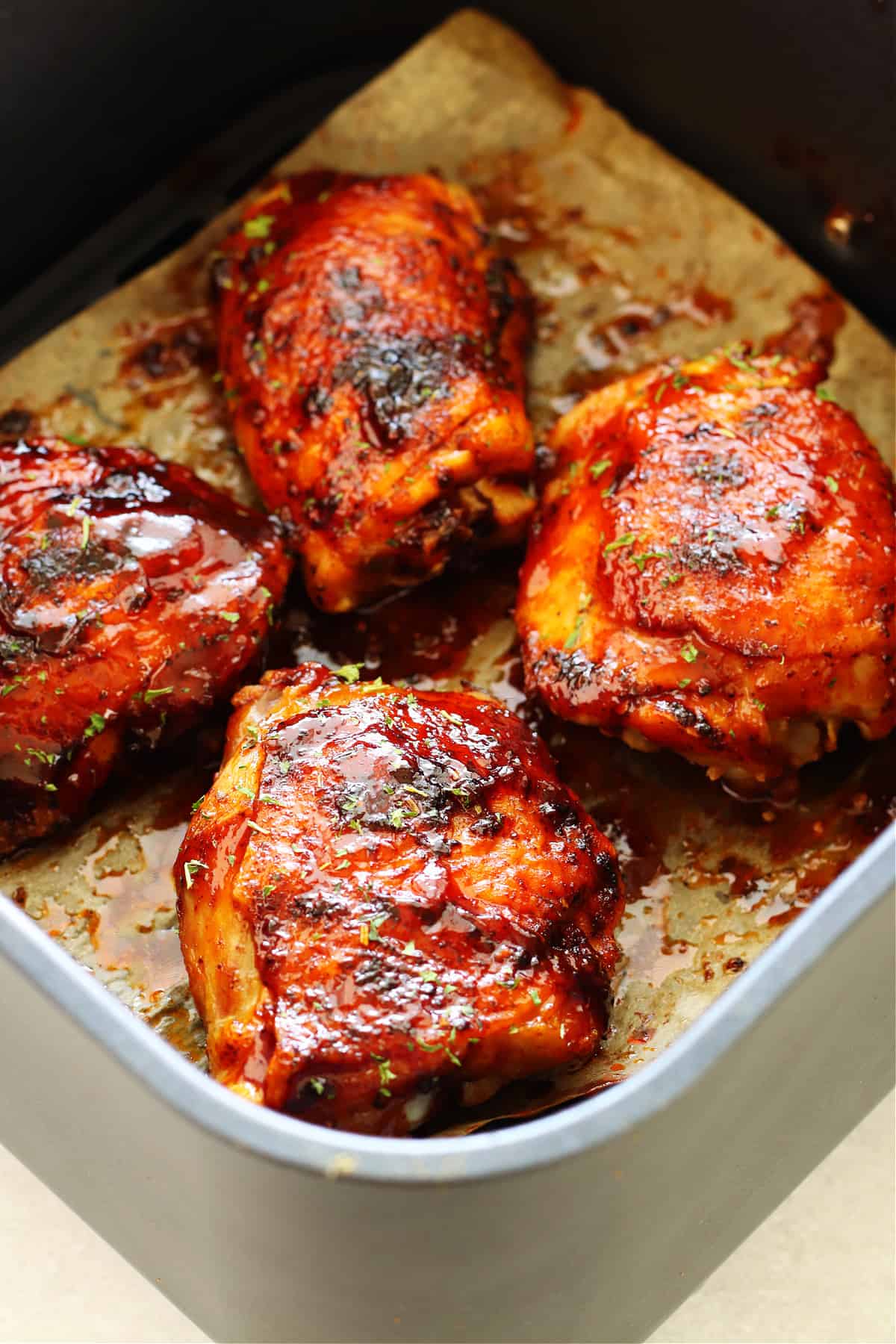 Air Fryer BBQ Chicken Thighs. Chicken thighs with BBQ sauce in the air fryer basket.