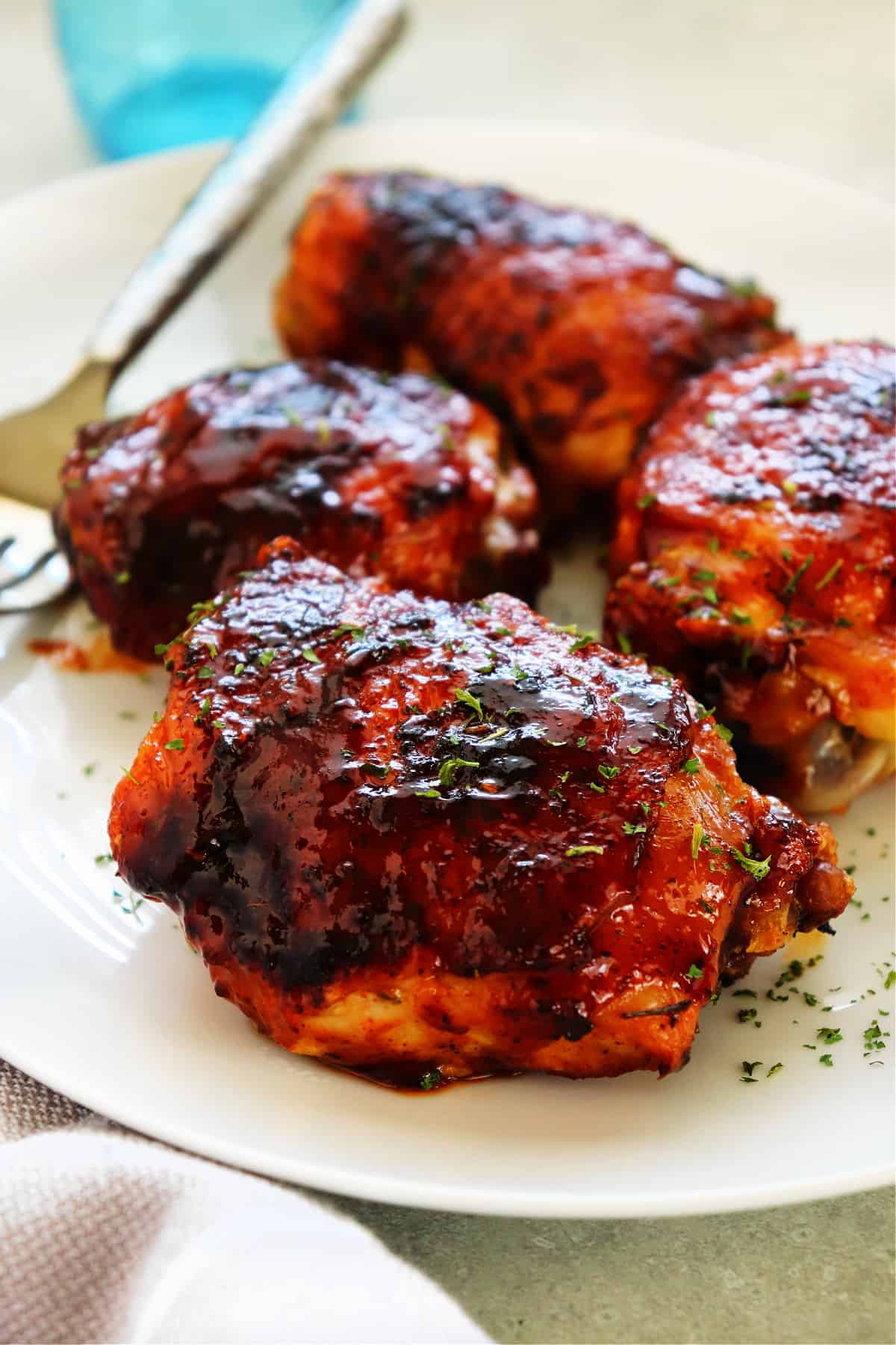 BBQ chicken thighs on white serving platter with fork.