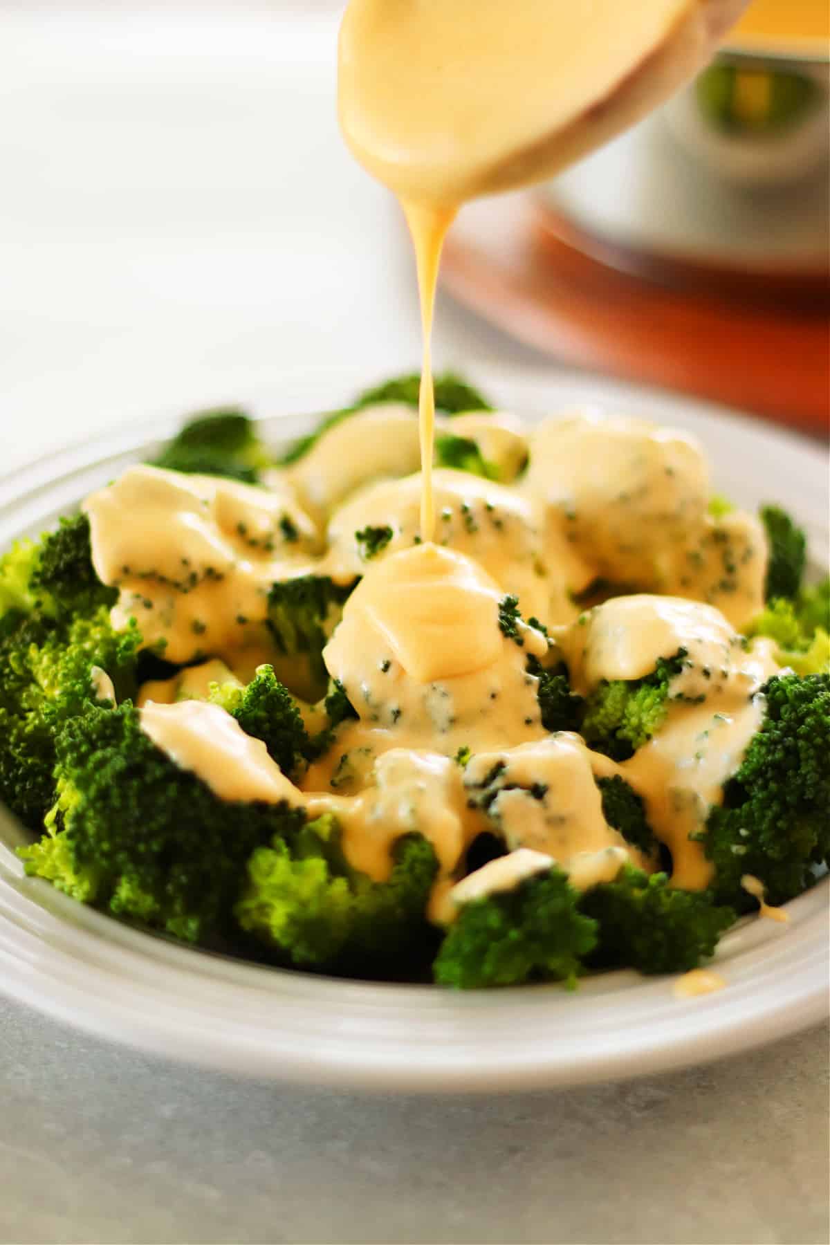 Cheddar cheese sauce drizzled over cooked broccoli in a bowl.