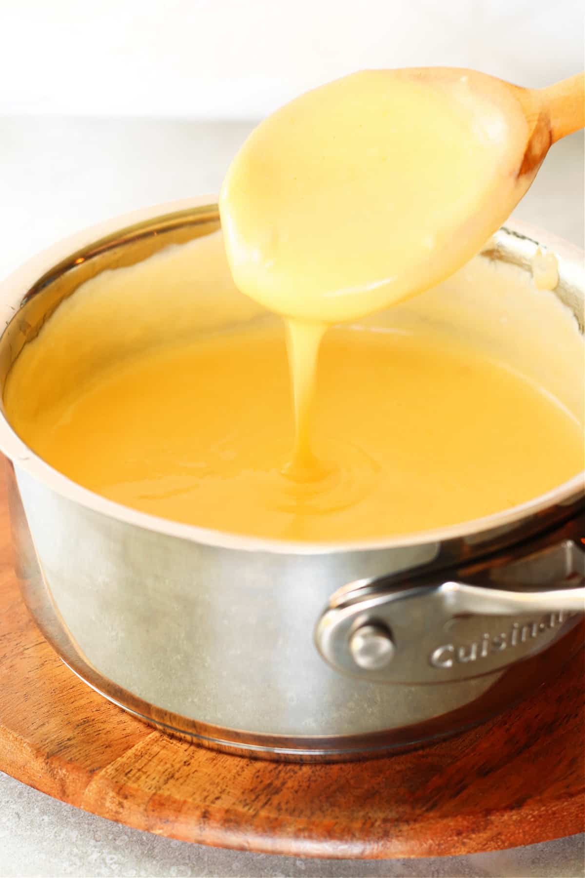 Cheese sauce in a saucepan drizzled from wooden spoon.