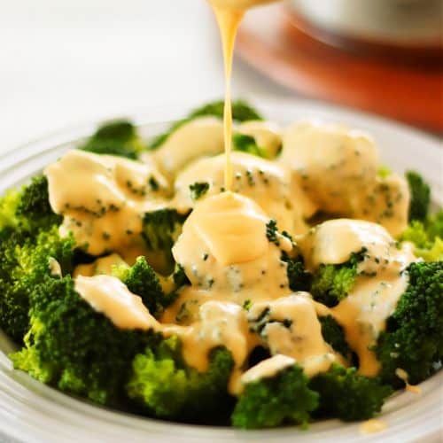 Close up shot of cheese sauce being poured over broccoli.