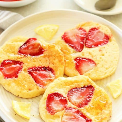 Pancakes with strawberry slices on a cream plate with fork.