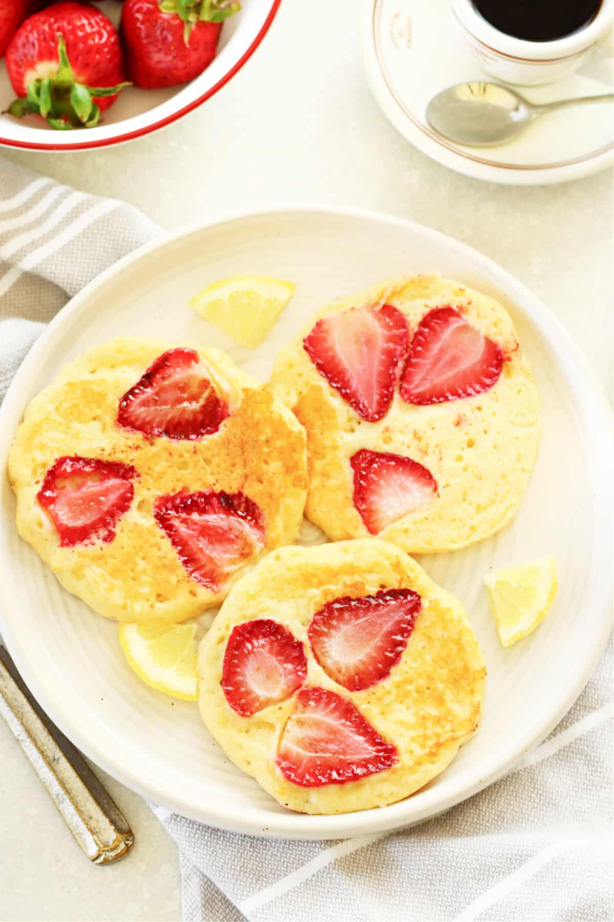 Three pancakes with strawberries on a cream plate.
