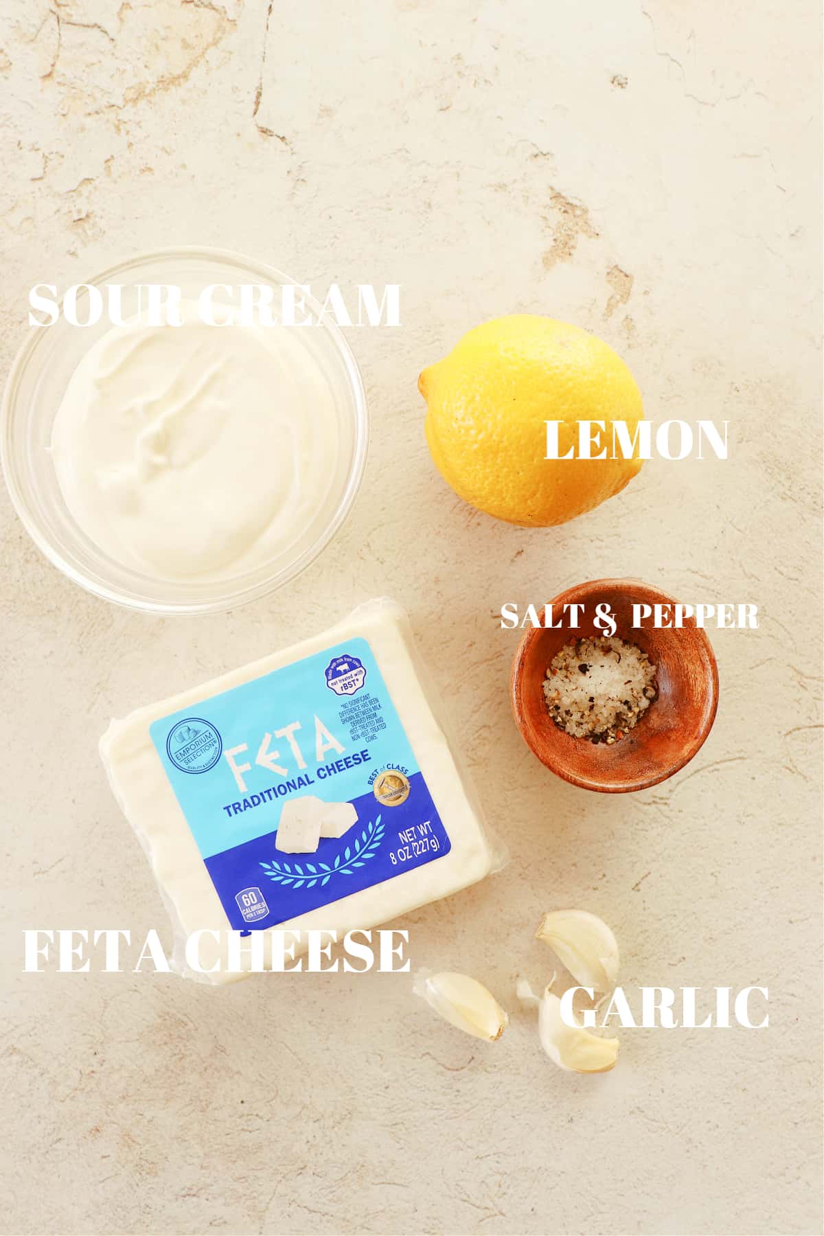 Feta, sour cream, lemon, garlic and salt and pepper on a cream board.